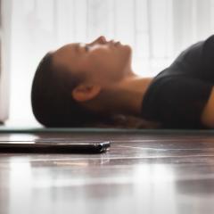 woman lying next to phone on yoga mat meditating